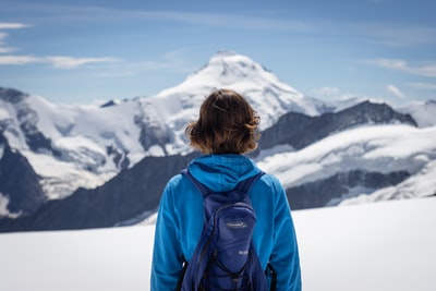 穿着蓝色夹克的女人白天看着白雪覆盖的山